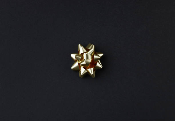 A golden bow on the black background. Minimalism gift decoration. Flat lay, top view