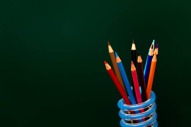 glass pot of coloured pencils close up, some in focus and others muted, blue backgrround