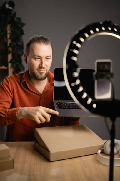 istock Handsome male blogger unboxing parcel with laptop on camera at home, taking computer out of box while recording video content for tech blog 1809350546