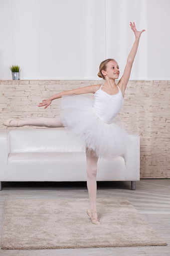 Girl in white ballet dress with ballet shoes standing in ballet pose.
