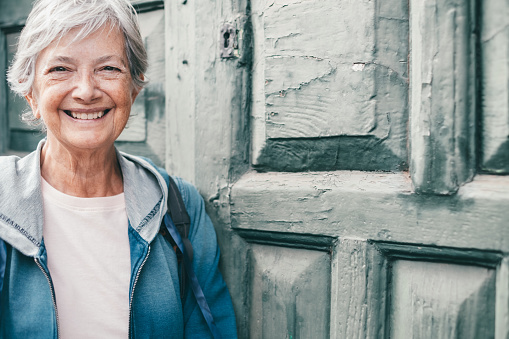 Portrait of caucasian senior smiling woman with short hair in outdoors looking at camera, old wooden door in background