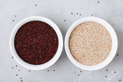 Quinoa grains. Red and white dried quinoa seeds in bowl on gray stone background, top view.
