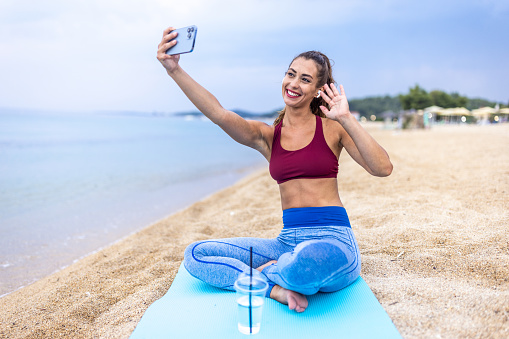 Sporty woman with headphones using her smart phone while relaxing after morning workout at the beach.