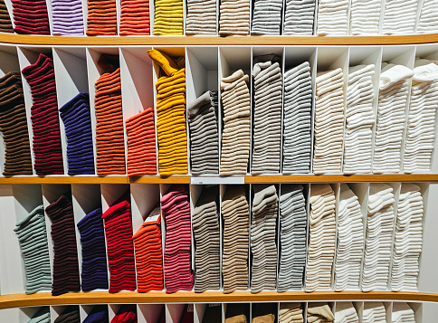 A variety of colorful socks on display and for sale in the clothing store. The garments are neatly stacked on wooden shelves.