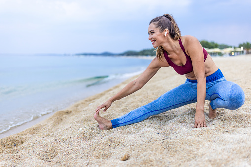 A beautiful young woman is doing stretching exercise at the beach in summer morning.