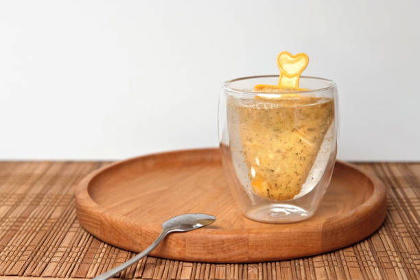 Brew iced tea on a stick in a modern transparent glass mug. Buckthorn, orange, mango fruit beverage. Trendy nordic tea 2024. Trend of Drink. Frozen berry mash smoothie on a stick brewed with hot water