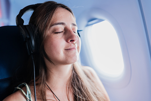 Young woman listening to music with headphones during plane trip