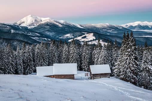 Three abandoned log cabins at beautiful sunrise or sunset in winter Carpathian mountains