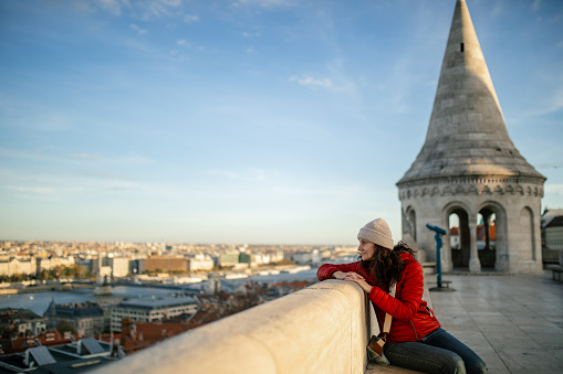 Woman at Fisherman's bastion in Budapest, sitting, enjoying the view, looking happy and relaxed.\nIt is one of the most important monument and tourist and well known tourist attractions due to the unique panorama of Budapest. This famous current structure are built between 1895 and 1902.