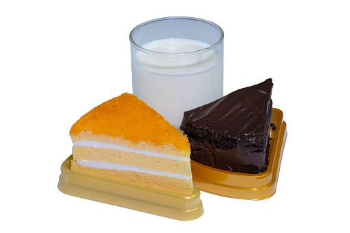 Glasses of white milk, chocolate cake and orange cake lined up against an easily distinguishable white background.