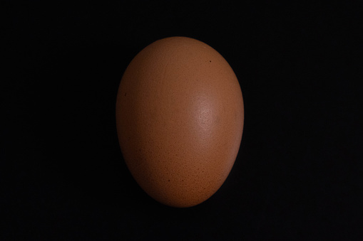 A single chicken egg sits on an easily distinguishable black background. Can be used for cooking