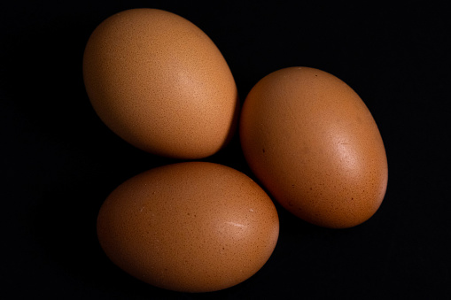 Three chicken eggs lay on an easily distinguishable black background. Can be used for cooking
