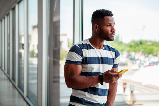 istock Young African American man looking out a window with cellphone in hand 1809434175