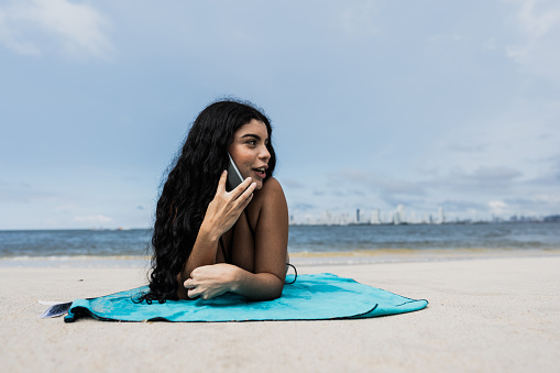 Young woman talking on mobile phone and lying on beach towel