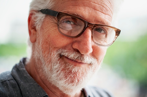 Side-lit mid-shot front view of amused senior man looking directly at camera
