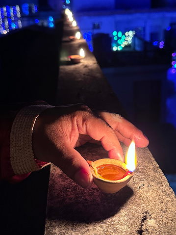 Stock photo showing close-up, elevated view of wall top with row of lit diya (oil lamp), with flickering flames in the dark, part of Diwali festival of lights celebration.
