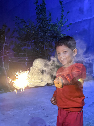 Stock photo of young Hindu boy in casual clothing and Indian man dressed in kurta traditional clothing in front of house decorated with multicolour fairy lights. They are both holding lit sparklers to celebrate Diwali, the Indian traditional festival of lights.