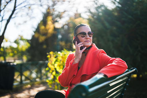 Woman sitting on a park bench, using mobile phone.