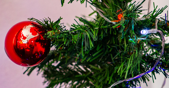 A red Christmas Bulb and Christmas lights hanging in an artificial Christmas tree.