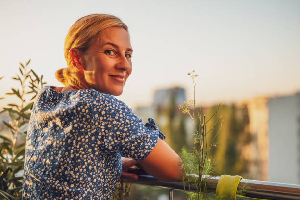 Woman enjoys standing on her balcony at sunset Beautiful woman enjoys standing on her balcony at sunset. apartment balcony garden stock pictures, royalty-free photos & images