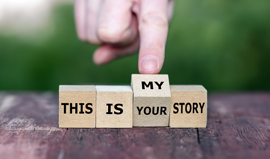 Hand turns wooden cube and changes the expression 'this is your story' to 'this is my story'.