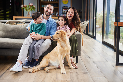 Portrait of smiling parents and their two adorable little children sitting with their family golden retriever in their living room at home