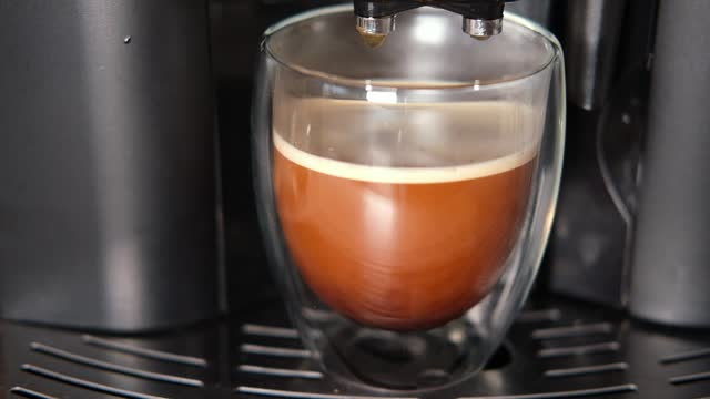 Espresso Pouring from Coffee Machine into Transparent Double Wall Glass Cup. Preparing Fresh Black Americano. Morning Coffee Brewing Preparation. Professional Electric Automatic Kitchen Coffee-Maker.