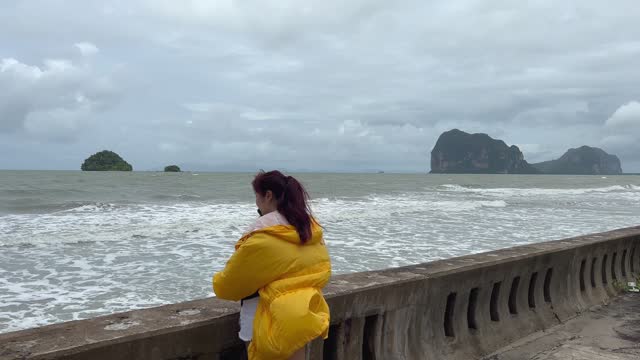 Woman in yellow jacket using smartphone on coastline with storm cloud and rain falling on sea