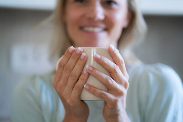 Caucasian female is holding a coffee mug in hands.