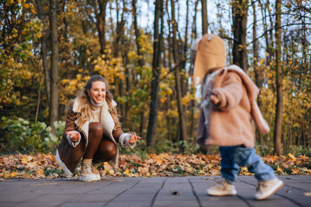 une petite fille mignonne et heureuse fait ses premiers pas sous l’œil attentif d’une mère bienveillante - baby first steps autumn child photos et images de collection