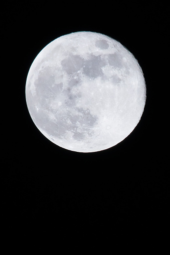 Stock photo showing a full moon shining against a black, night time, starless sky.