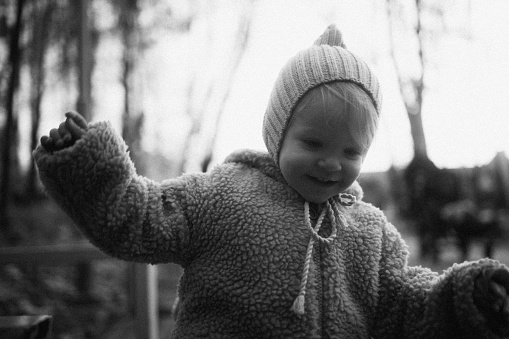 This black and white portrait beautifully captures the happiness of a baby girl in the serene setting of an autumn park, emphasising the timeless and classic charm of the moment