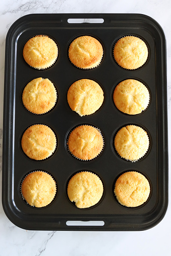 Stock photo showing close-up, elevated view of cake tray of freshly baked homemade vanilla cupcakes in paper cases cooling down ready to eat. Home baking concept.