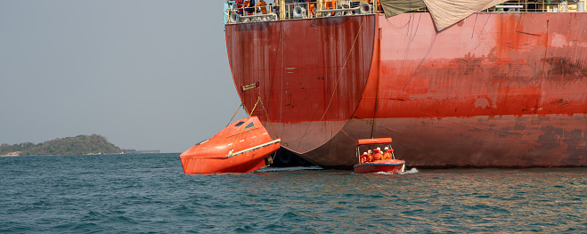 Watertight lifeboat test. Port state control. Lowering orange totally enclosed lifeboat to water. Abandon ship drill. Lifeboat training.