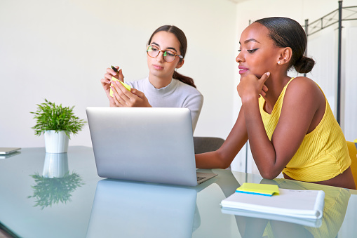 Two girls who work in a digital marketing company work as a team in a coworking with their laptop and smartphones