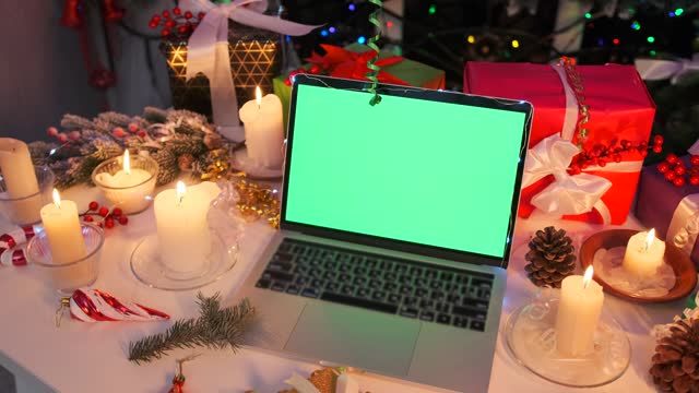Laptop with blank green screen for Christmas holiday advertisement on table decorated with gift boxes