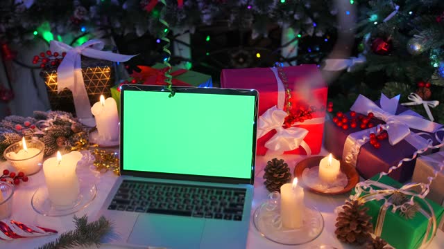 Close up, laptop computer with green screen near warm candlelight, gifts, presents
