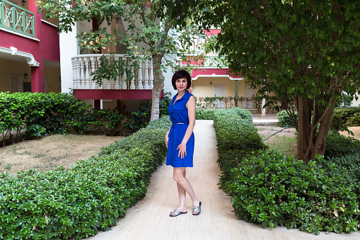 Adult brunette woman blue dress in a city garden.
