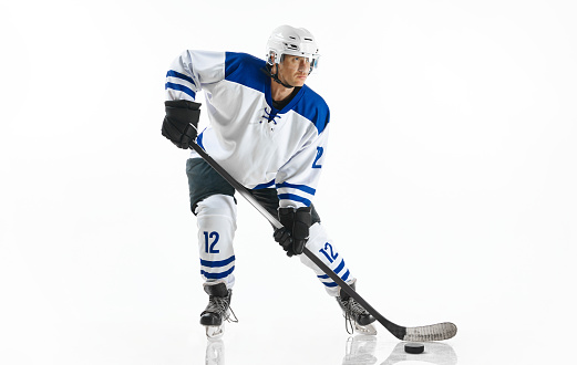 Concentrated young man, hockey player in uniform standing with stick on nice rink against white studio background. Concept of professional sport, competition, game, tournament, game, action