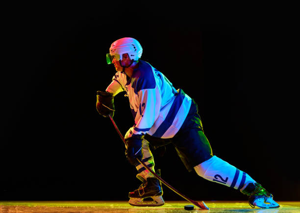 istock Side view. Athlete, man, ice hockey player during game in motion with stick against black studio background in neon light 1809600293
