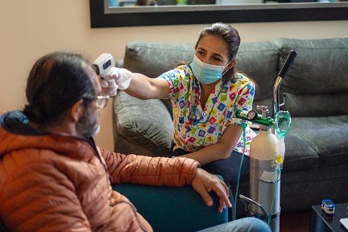 Nurse checks the temperature with an infrared thermometer of a Latino male, the male is seated in the room while his body temperature is measured.