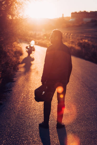 istock Motorcyclist standing on the road at sunset 1809604726