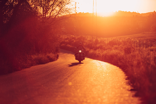 Solo motorcyclist riding his motorcycle with his light on at sunset on a narrow road