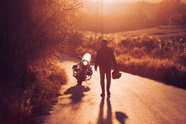 istock Motorcyclist walking on the road at sunset 1809604798
