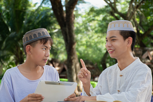 Asian muslim boys sit together in school park to read and learn their daily activity and do homework in their free times before going back home, soft and selective focus.