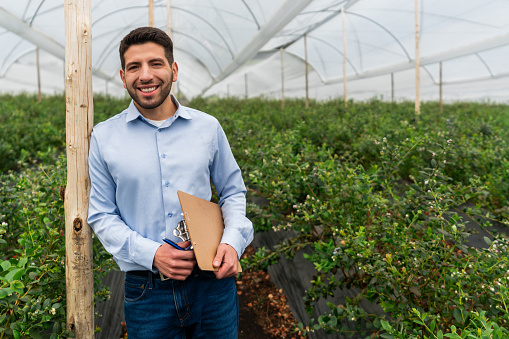 Portrait of a happy agronomist working at a blueberry plantation and looking at the camera smiling - agriculture concepts
