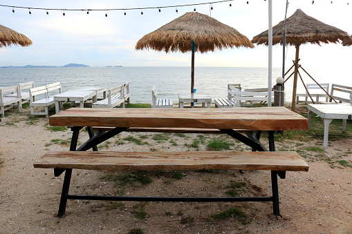 Brown wood table and bench on sand with sea and bright sky background, Thailand.