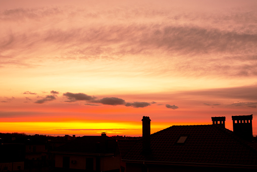 Roofs of houses against the backdrop of a beautiful sunset. Orange sky with beautiful cumulus clouds. Textured sky background at sunset.