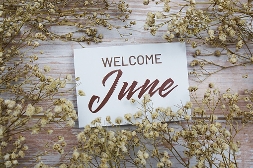 Welcome June text on paper card with flower decoration on wooden background