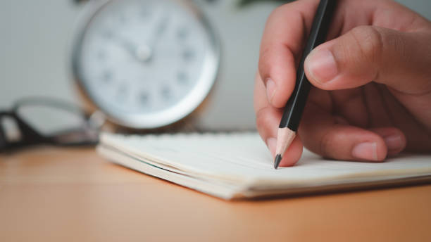 istock Human hands writing notes with pencil on paper on wooden table surface. 1809652558